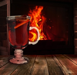 Mulled wine in glass cup on wooden table near fireplace
