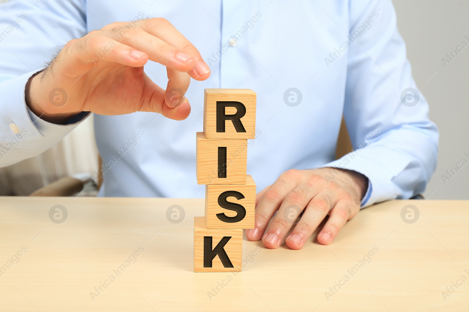 Photo of Businessman destroying tower of cubes with word Risk at table, closeup