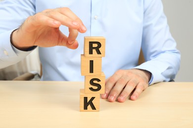 Photo of Businessman destroying tower of cubes with word Risk at table, closeup