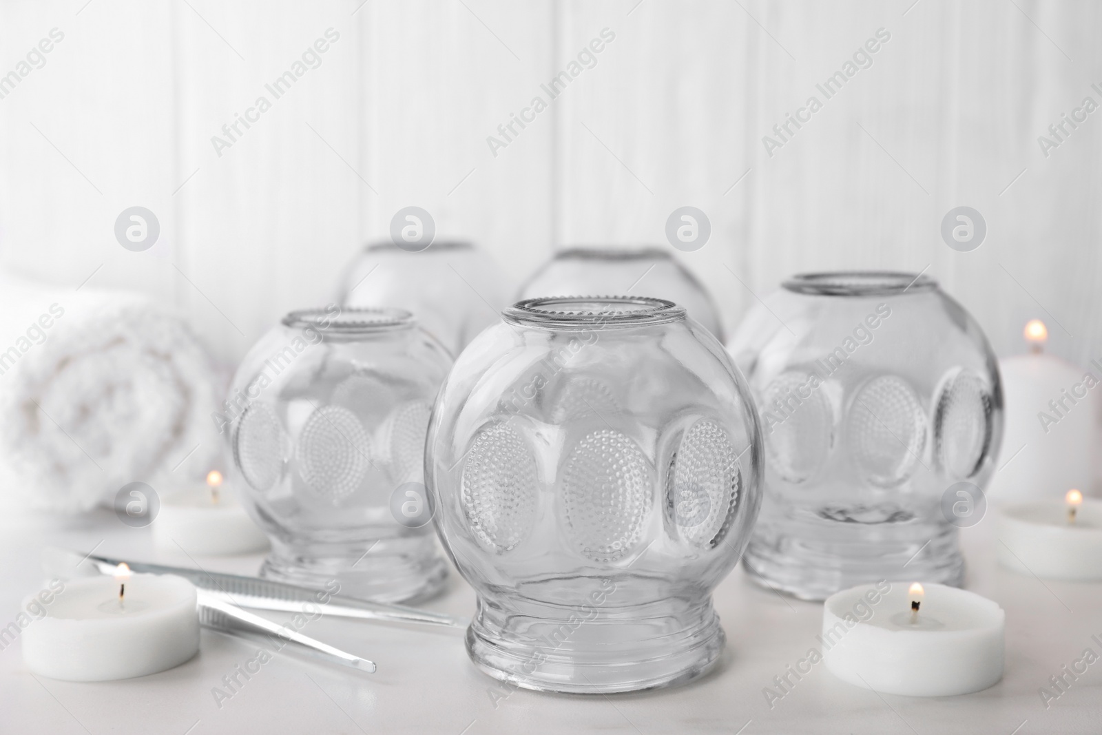 Photo of Glass cups, burning candles and tweezers on white table. Cupping therapy