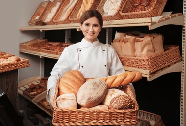 Photo of Professional baker with tray full of fresh breads in store