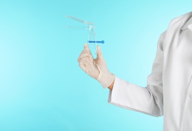 Photo of Male doctor holding disposable speculum on color background, closeup with space for text. Medical object