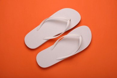 Stylish white flip flops on orange background, top view