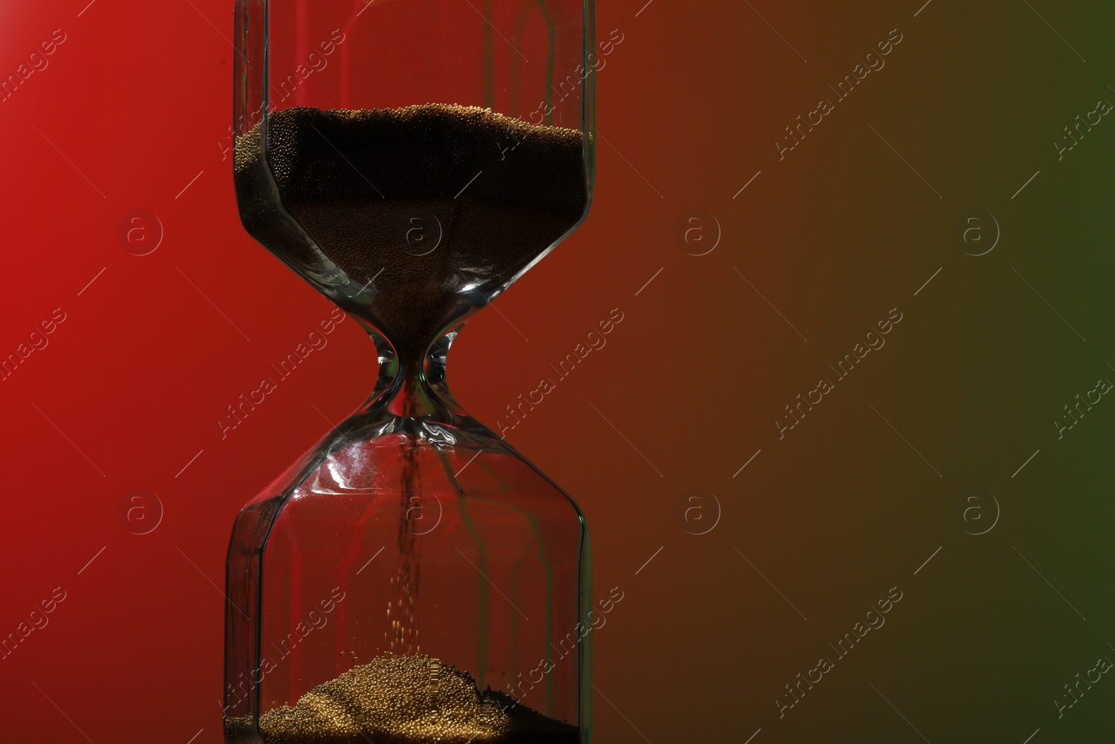 Photo of Hourglass with flowing sand on color background. Space for text