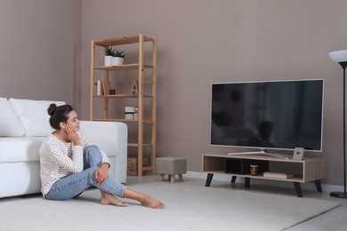 Photo of Woman watching television at home. Living room interior with TV on stand