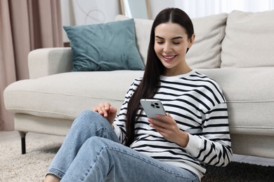 Happy young woman using smartphone at home