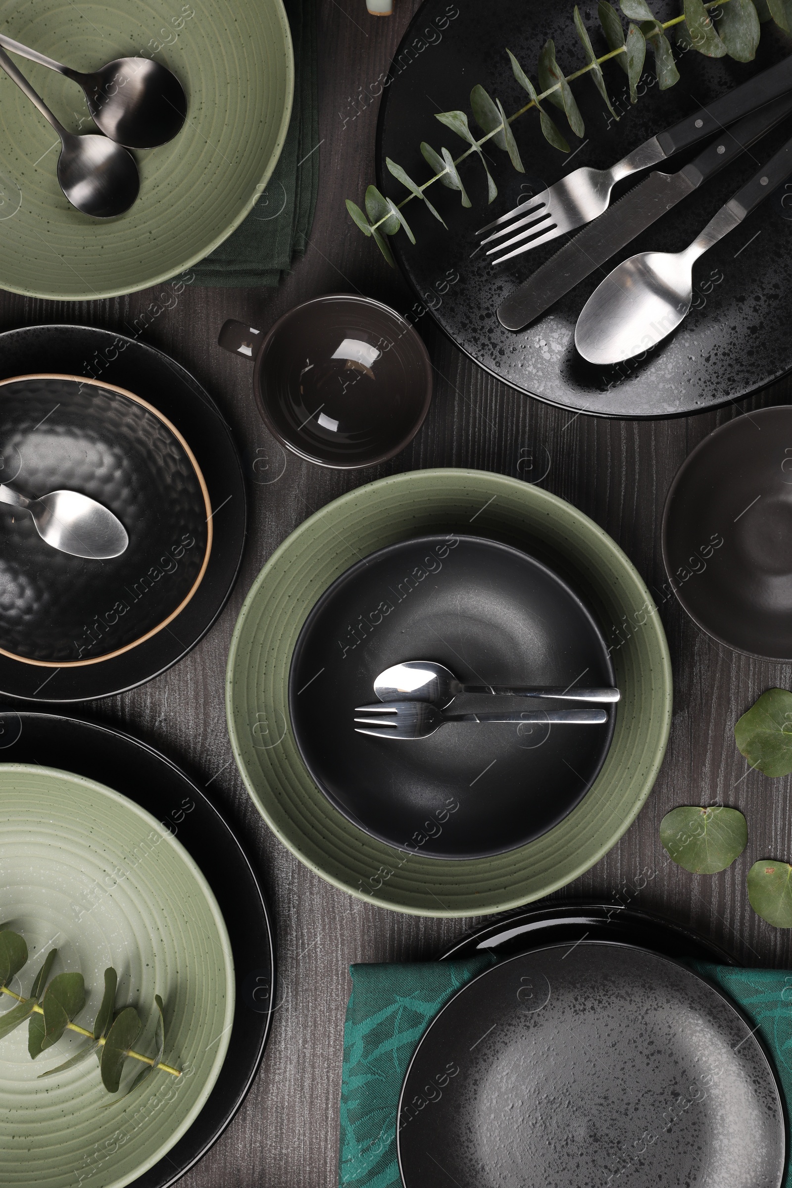 Photo of Stylish table setting with cutlery and eucalyptus branches on dark wooden background, flat lay