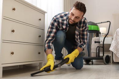 Photo of Man vacuuming floor under chest of drawers indoors