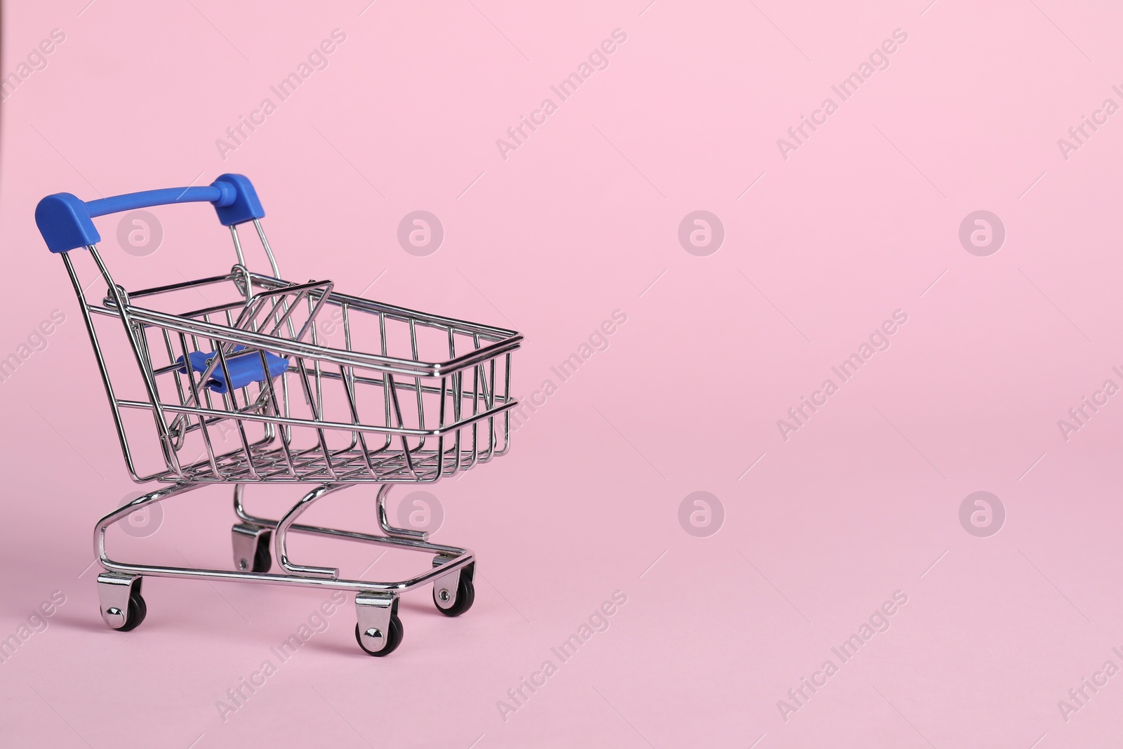 Photo of Small metal shopping cart on pink background, space for text