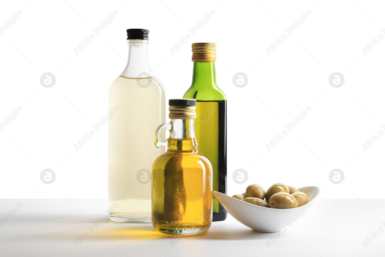 Photo of Bottles of different cooking oils and olives on white background