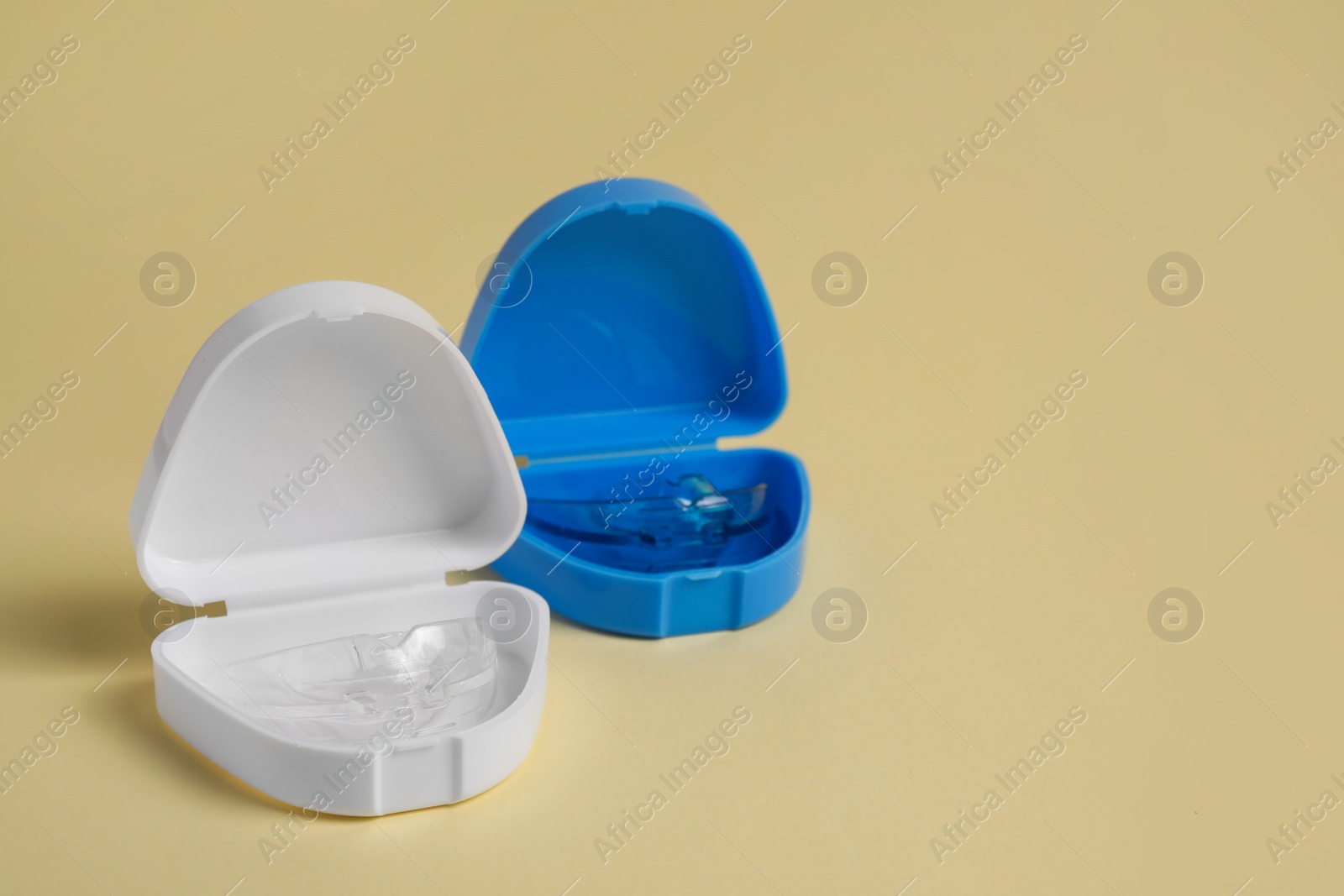 Photo of Transparent dental mouth guards in containers on beige background, space for text. Bite correction