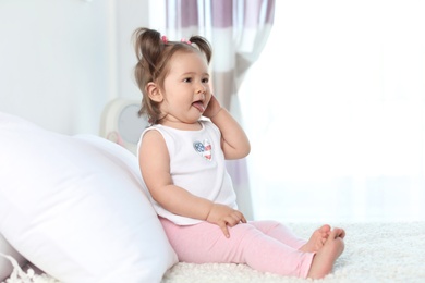 Adorable little baby girl sitting on bed in room. Space for text
