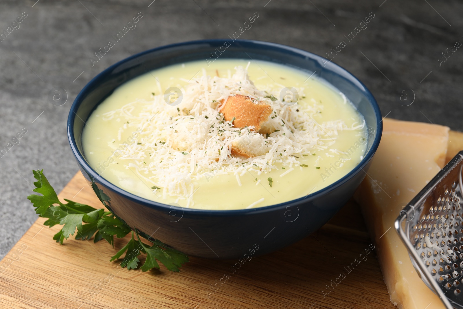 Photo of Delicious cream soup with parmesan cheese and croutons in bowl on grey table, closeup
