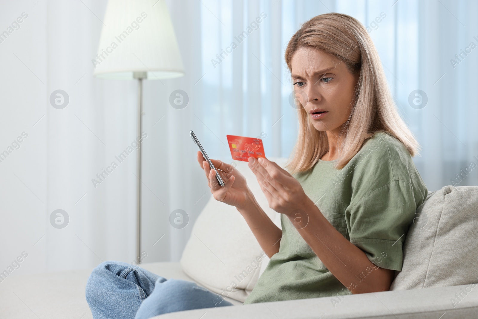 Photo of Stressed woman with credit card and smartphone at home. Be careful - fraud