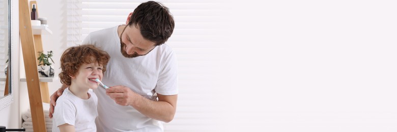 Image of Father helping his son to brush teeth in bathroom. Banner design with space for text