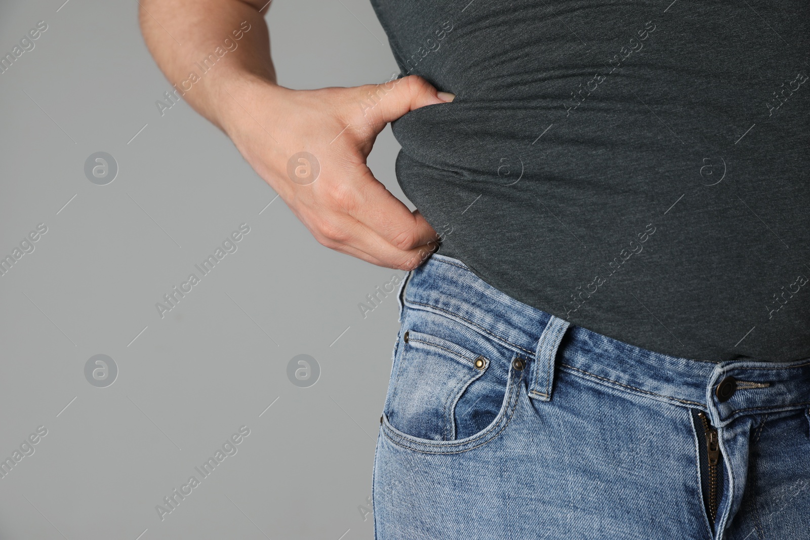 Photo of Overweight man in tight tshirt and jeans on light grey background, closeup. Space for text