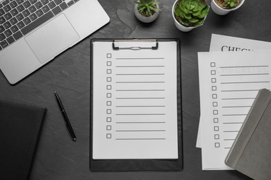 Photo of Clipboard with checkboxes, pen and laptop on black table, flat lay