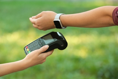 Photo of Woman using terminal for contactless payment with smart watch outdoors