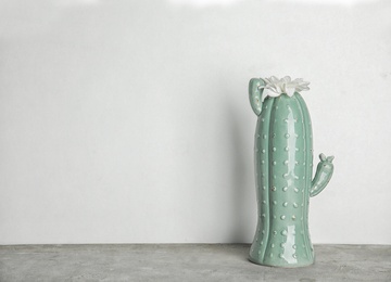 Trendy cactus shaped vase with flower on table against light wall. Creative decor