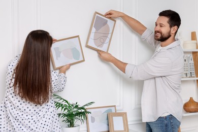 Photo of Man and woman hanging picture frames on white wall at home