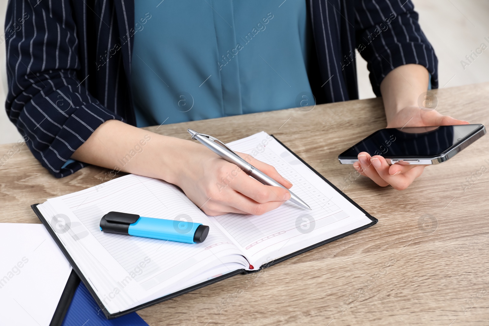 Photo of Woman taking notes while using smartphone at wooden table, closeup