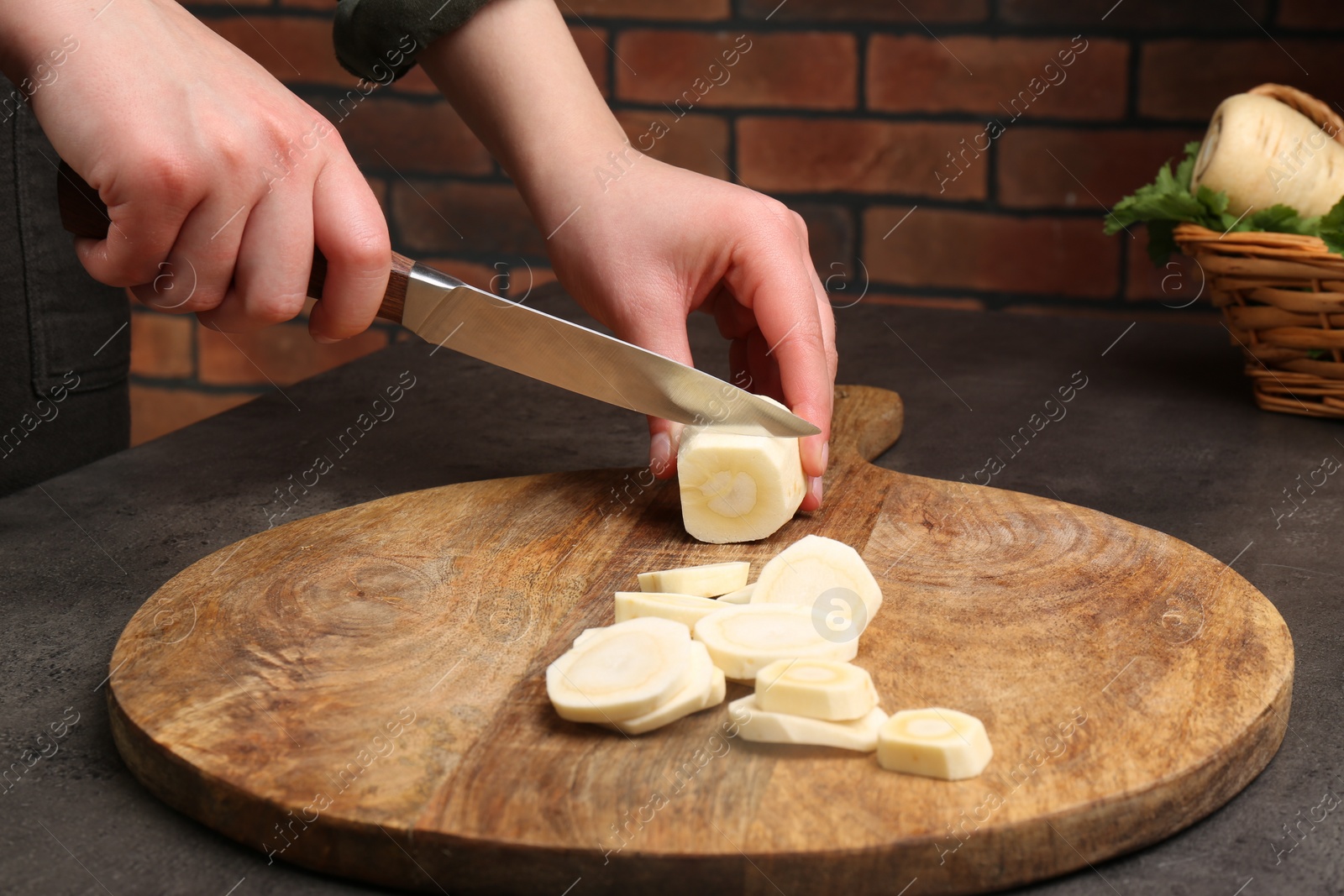 Photo of Woman cutting delicious fresh ripe parsnip at black table, closeup