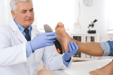 Photo of Male orthopedist fitting insole on patient's foot in clinic