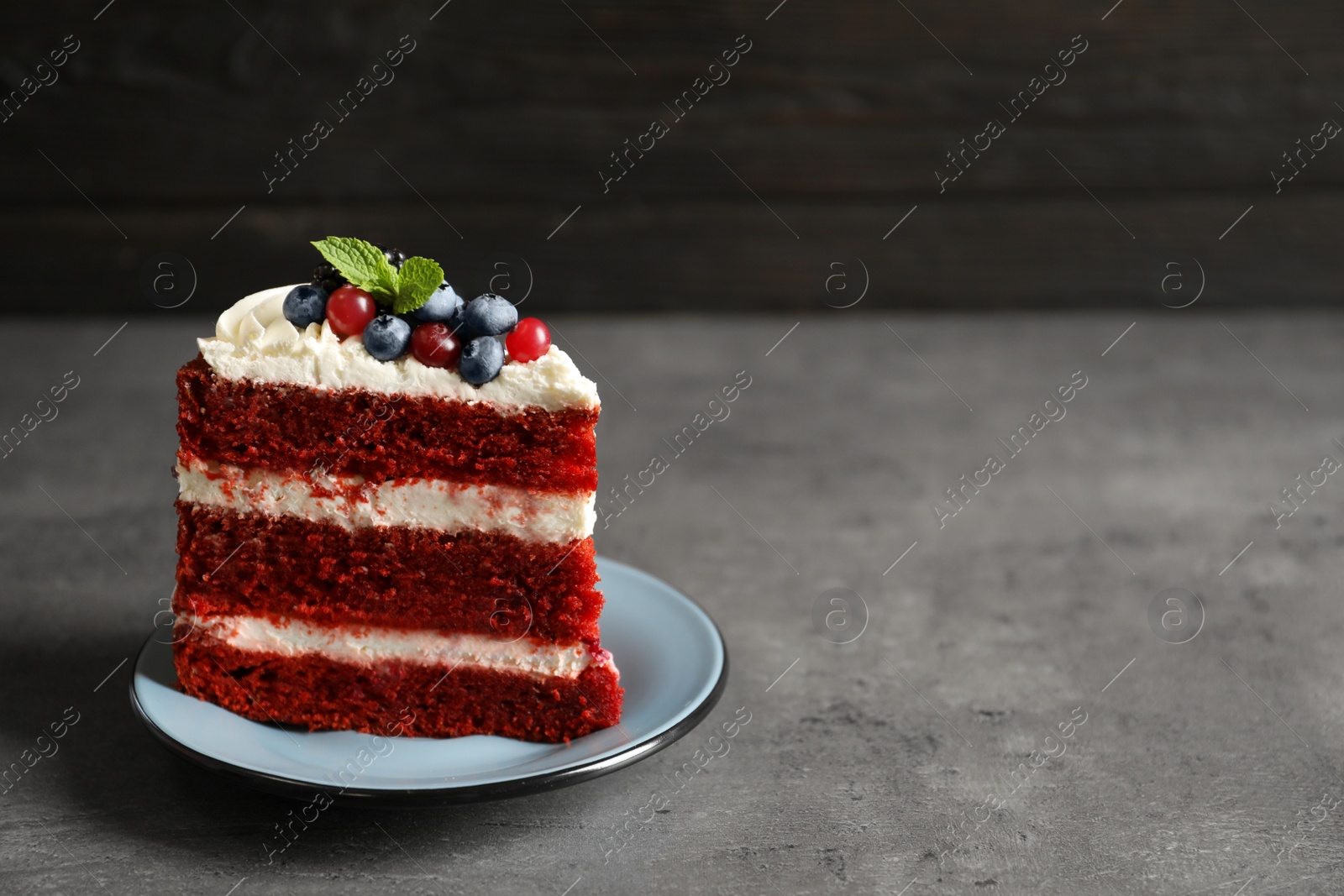 Photo of Plate with piece of delicious homemade red velvet cake and space for text on blurred background