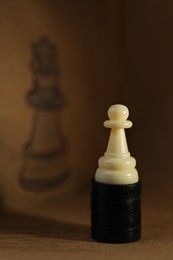 Photo of White pawn on wooden table in front of drawn queen chess piece