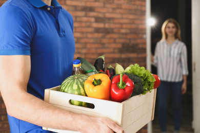 Photo of Courier with fresh products indoors, closeup. Food delivery service