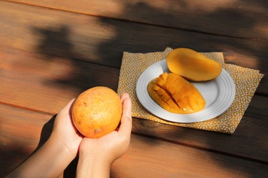 Photo of Woman holding tasty mango at wooden table, closeup