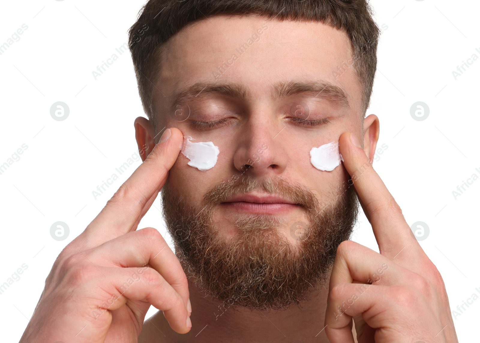 Photo of Handsome man applying moisturizing cream onto his face on white background