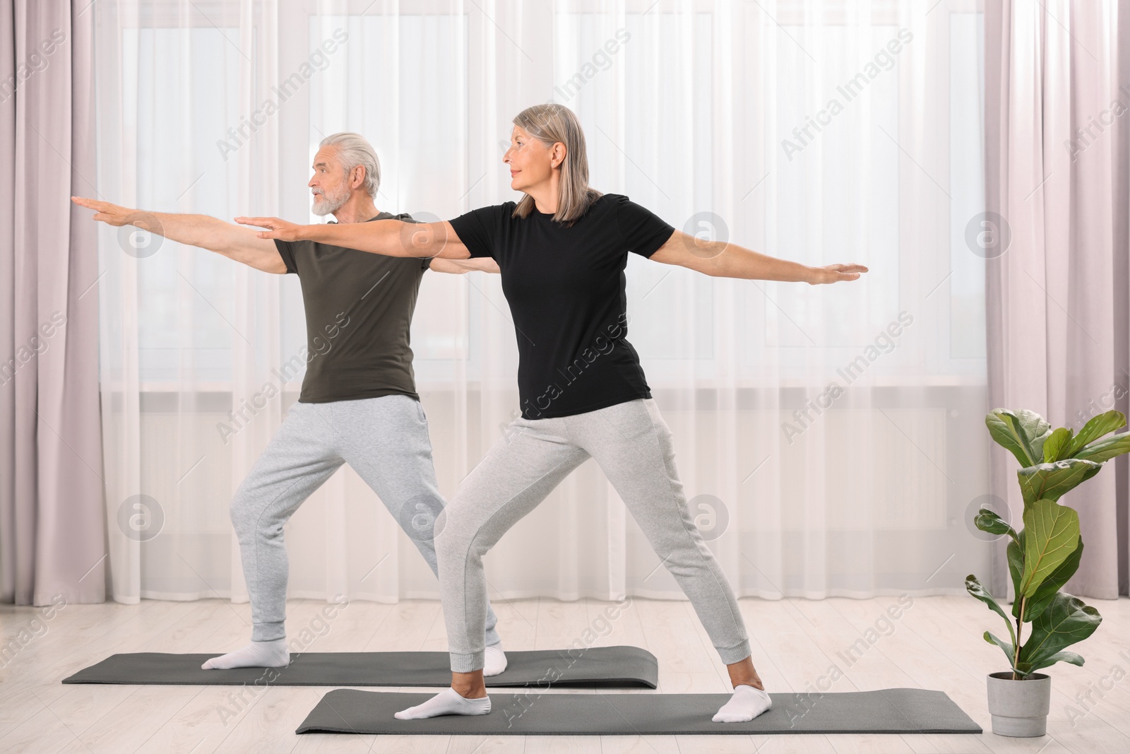 Photo of Senior couple practicing yoga on mats at home