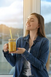 Beautiful young woman with delicious smoothie near window