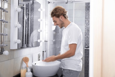 Photo of Young man washing hands in bathroom. Using soap
