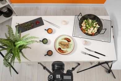 Photo of Professional camera on tripod and composition with delicious meat medallion in studio, above view. Food photography