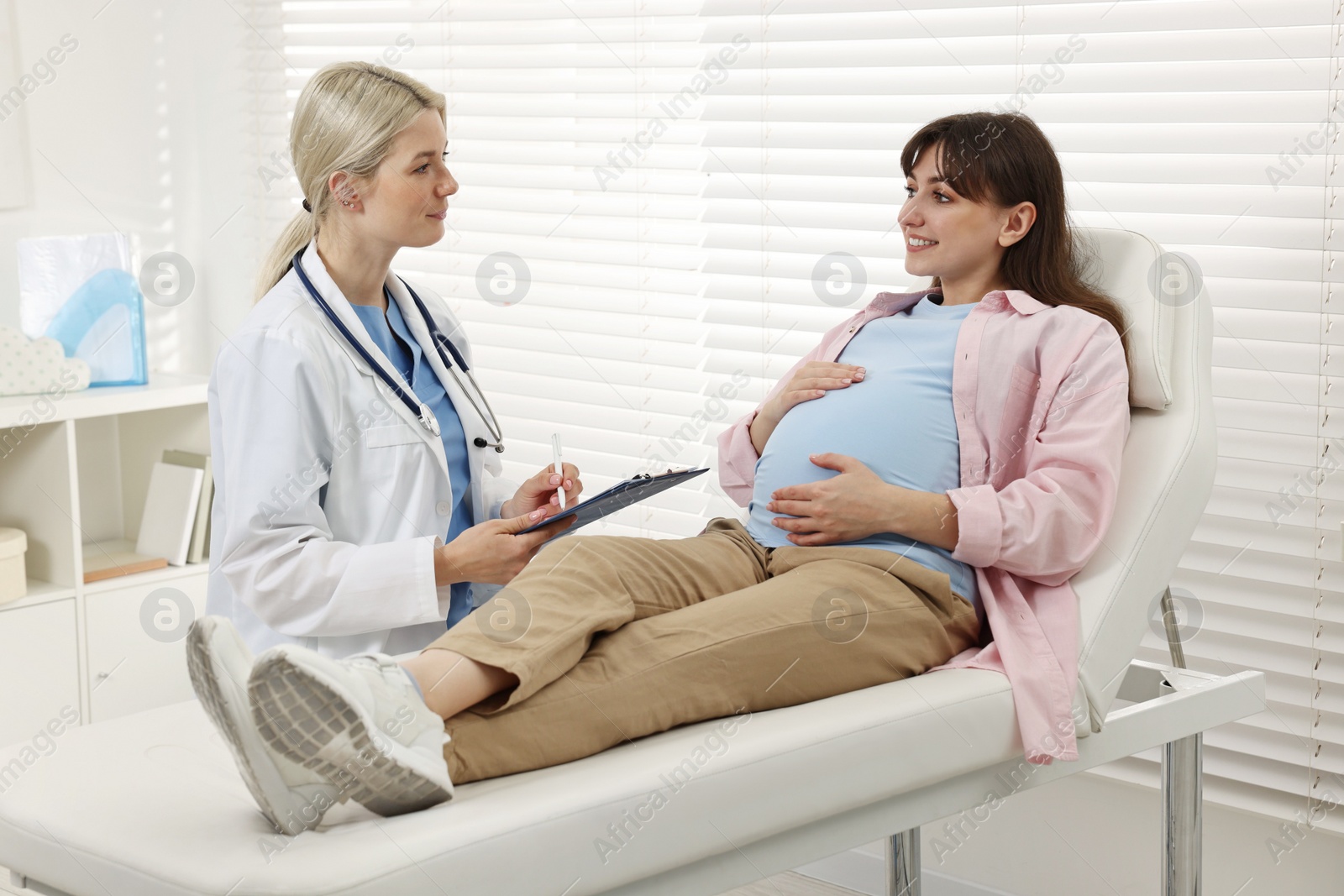 Photo of Doctor with clipboard consulting smiling pregnant patient in clinic