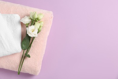 Photo of Soft folded towels with flowers on violet background, top view. Space for text