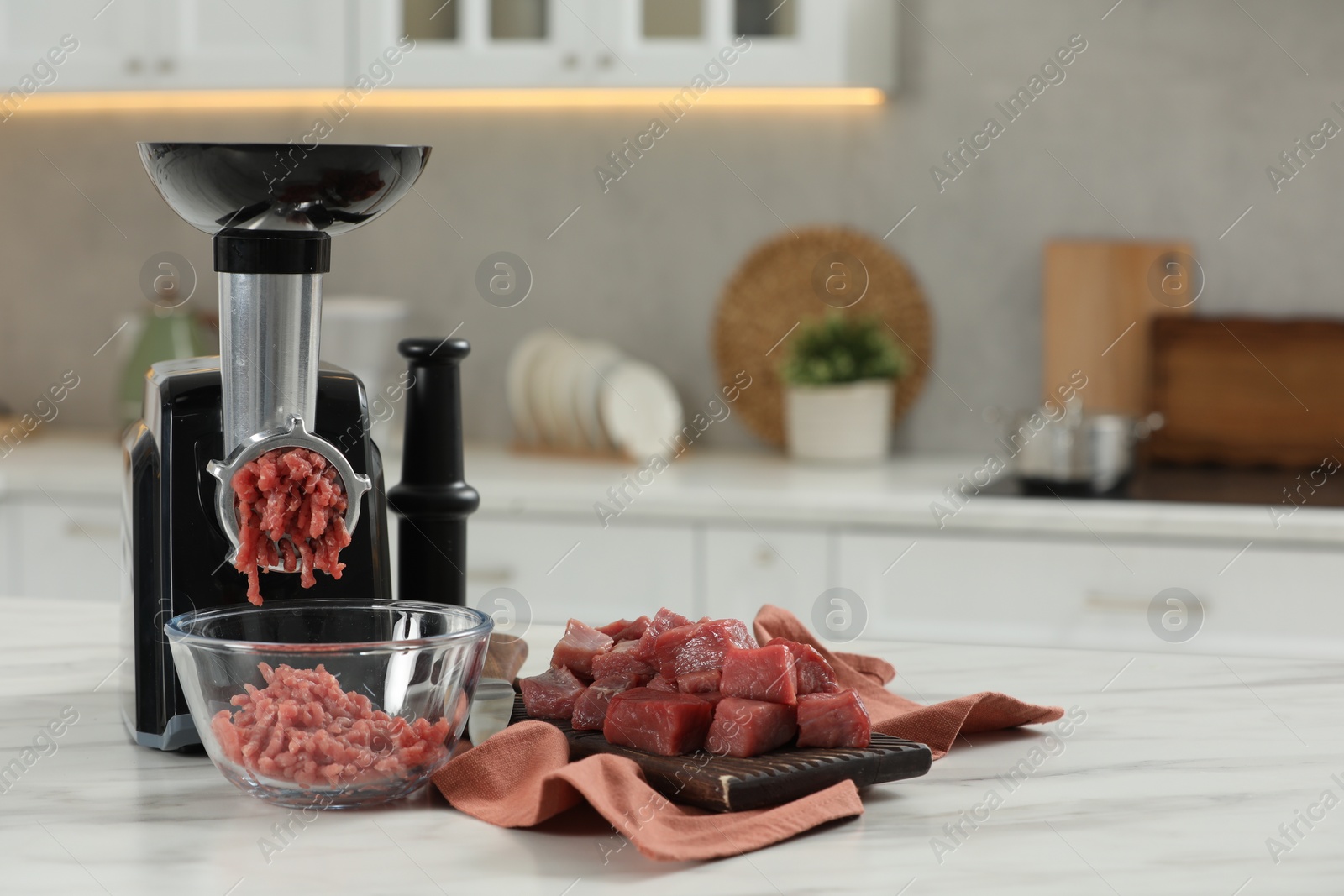 Photo of Electric meat grinder with beef mince on white table in kitchen, space for text