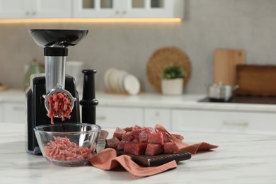 Photo of Electric meat grinder with beef mince on white table in kitchen, space for text