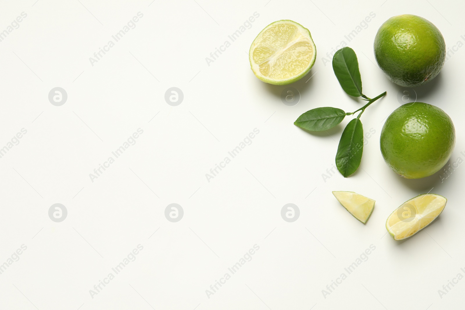 Photo of Whole and cut fresh ripe limes with green leaves on white background, flat lay