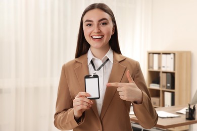 Happy woman pointing at blank badge in office