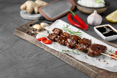 Photo of Skewers with pieces of tasty chicken meat glazed in soy sauce and other products on grey textured table, closeup. Space for text