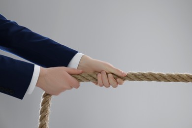 Photo of Dispute concept. Businessman pulling rope on light grey background, closeup