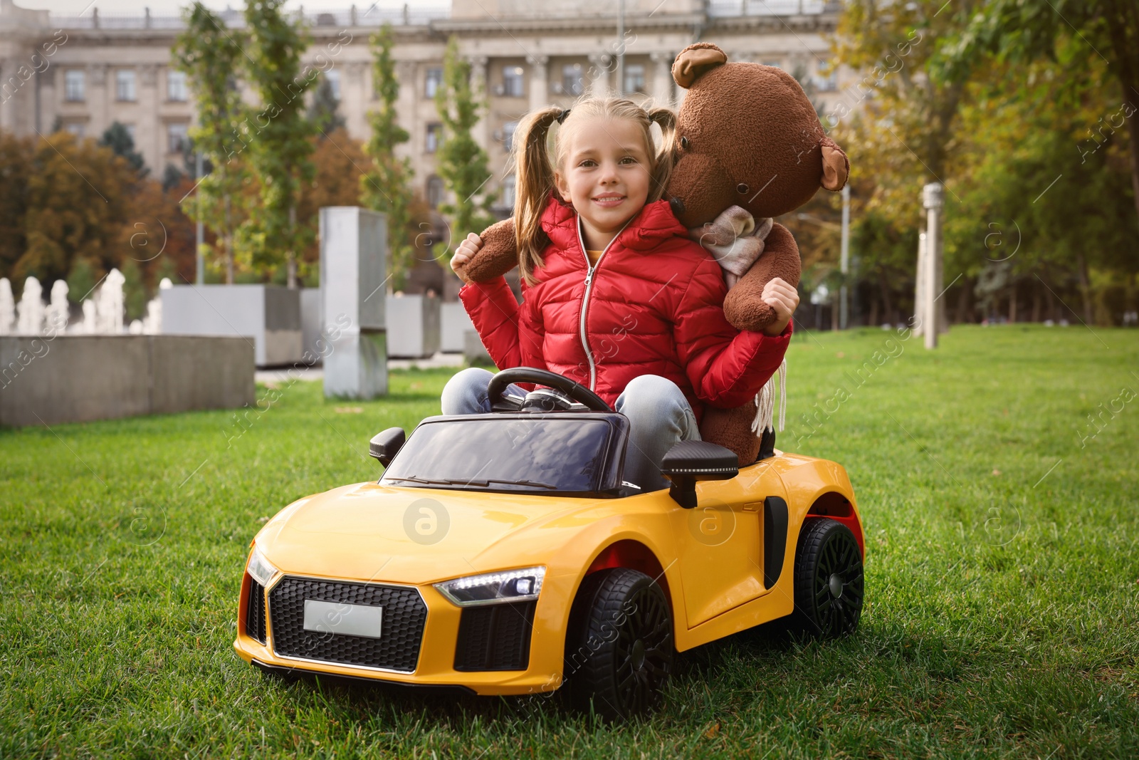 Photo of Cute little girl playing with toy bear and children's car in park