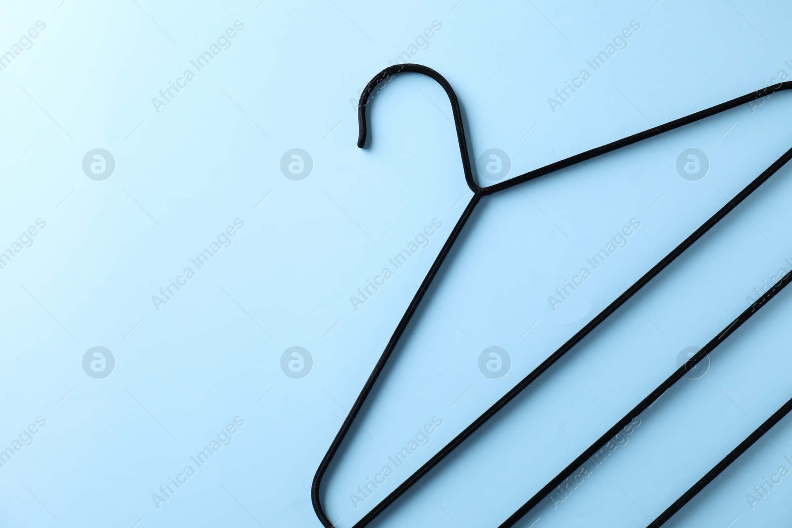 Photo of One black hanger on light blue background, top view. Space for text