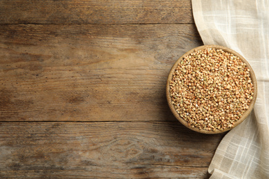 Photo of Uncooked green buckwheat grains in bowl on wooden table, top view. Space for text