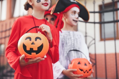 Photo of Cute little kids with pumpkin candy buckets wearing Halloween costumes going trick-or-treating outdoors, closeup