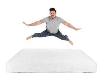 Young man jumping on mattress against white background