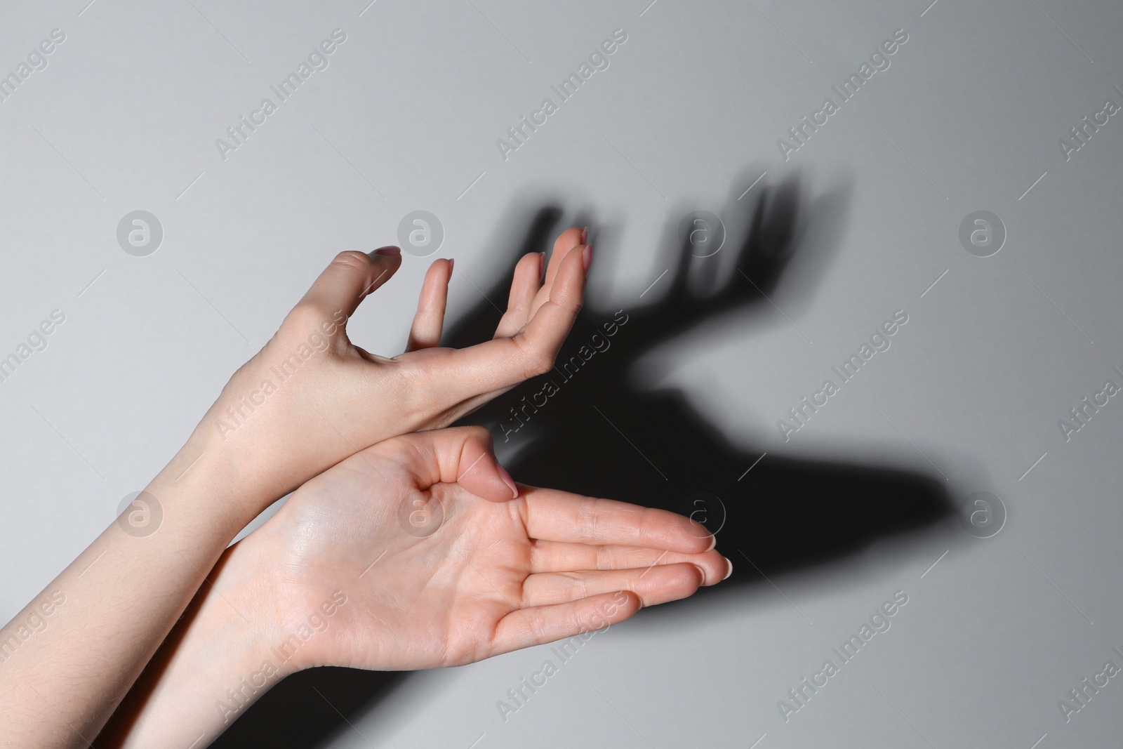 Photo of Shadow puppet. Woman making hand gesture like deer on grey background, closeup